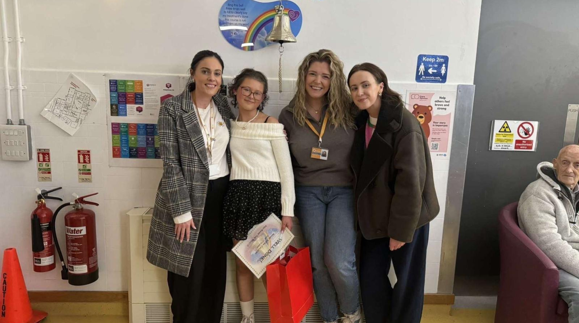 Keira smiling with Cancer Fund for Children staff after ringing the bell in the Royal Belfast Hospital for Sick Children to mark the end of her treatment