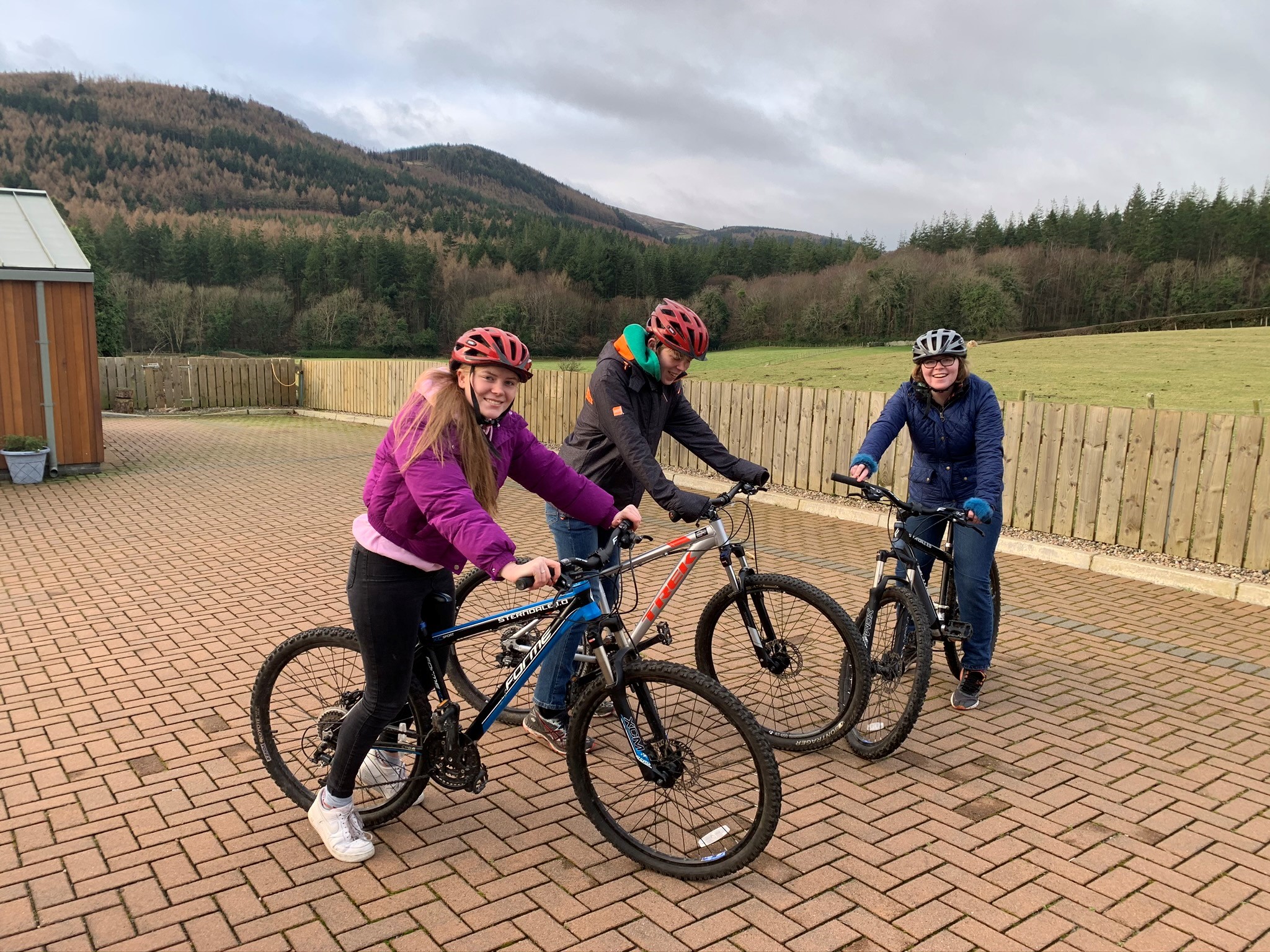 The image shows three teenagers on bikes. They are static and smiling at the camera with the Mourne mountains in the background.